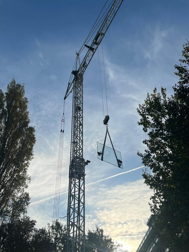 Bouwkraan hijst grote glasplaat met zuignappen naar bovenverdieping appartement Den Haag