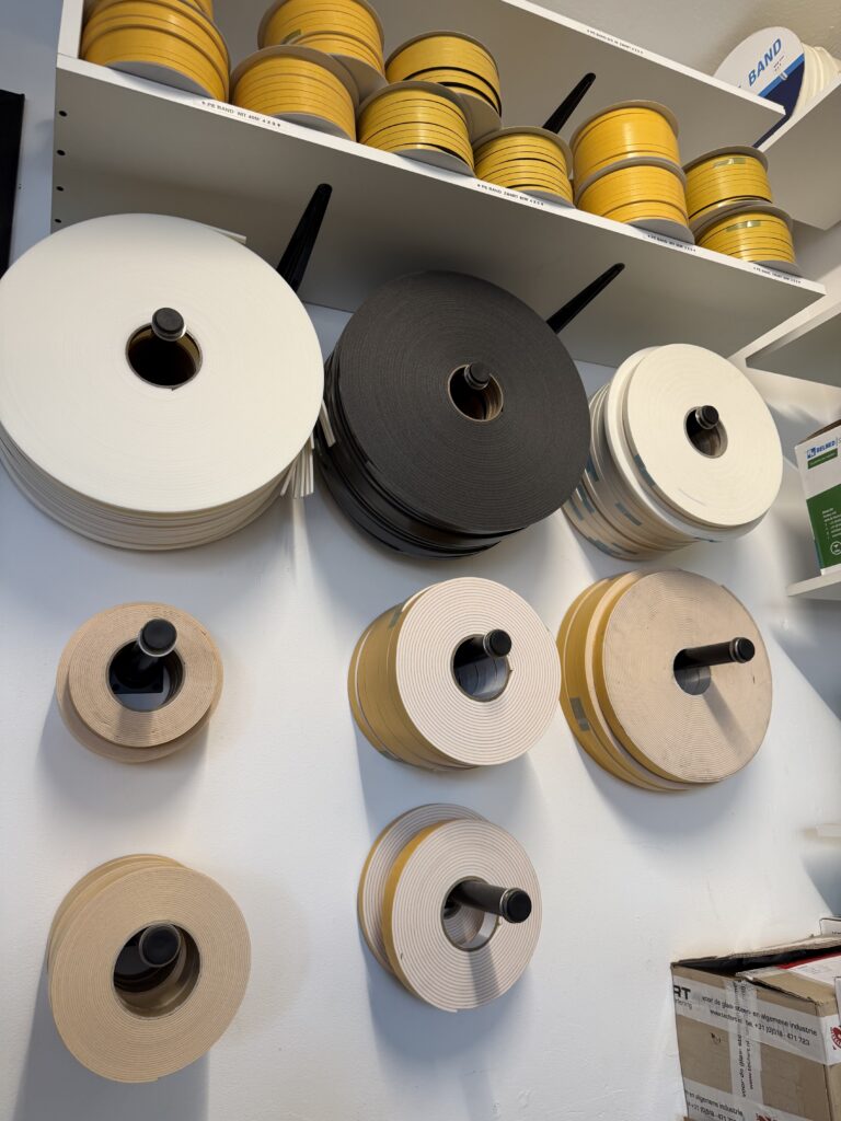 Glasband en schuimstrips in diverse kleuren op wandrek in werkplaats Glashandel Piket