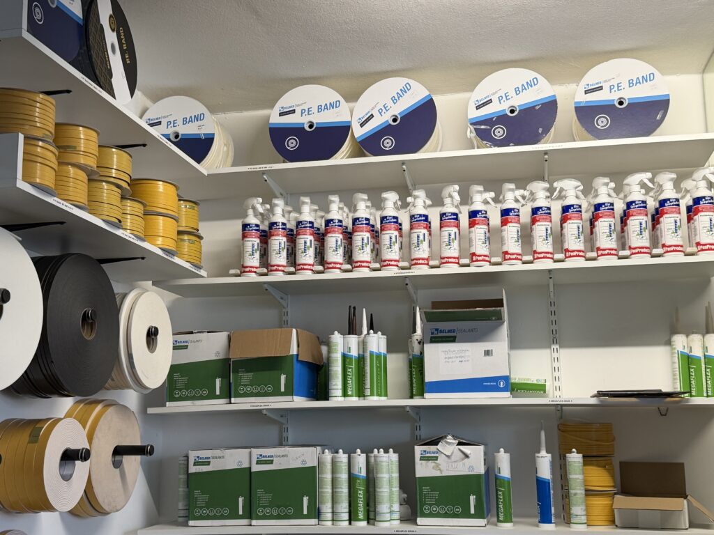 Werkplaats schappen met glasband rollen en Mega-Flex kittubes bij Glashandel Piket