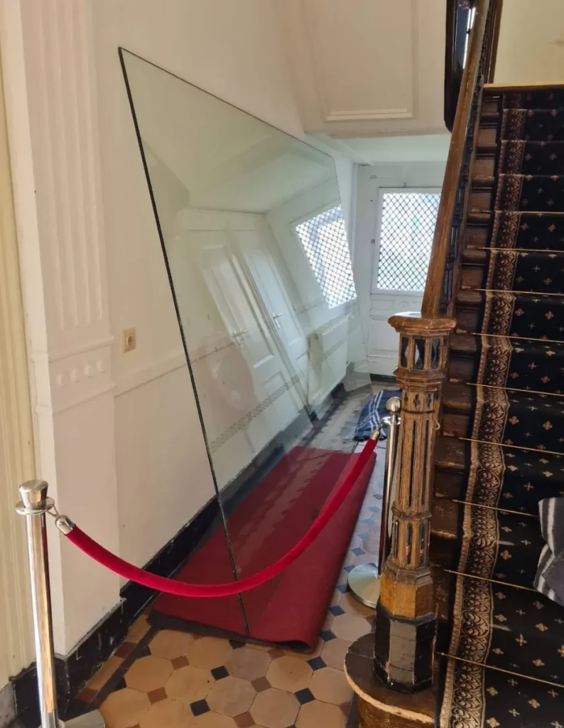 Glasplaat klaar voor plaatsing in hal van monumentaal pand met houten trap en betegelde vloer
